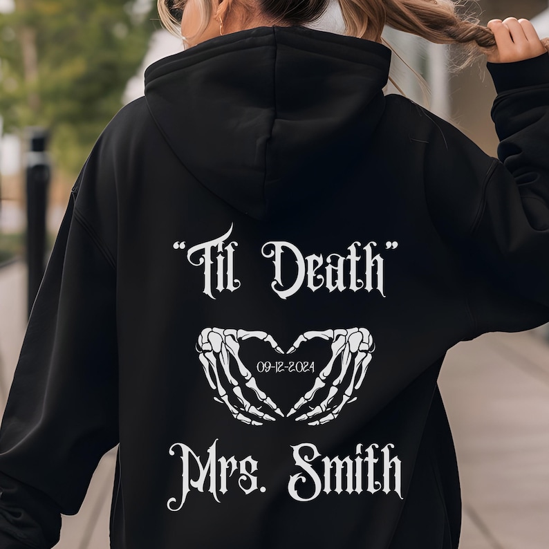 以下が含まれることがあります： 「Til Death」という白い文字と、ハートと日付「09-12-2024」と「Mrs. Smith」という文字が書かれた黒いフード付きスウェットシャツ。