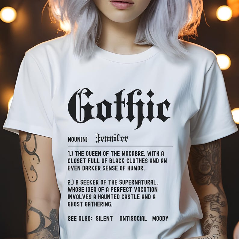 Puede incluir: Camiseta blanca con texto negro que dice "Gothic" y una definici&oacute;n de la palabra. La definici&oacute;n dice que "Gothic" es un sustantivo que significa "la reina de lo macabro, con un armario lleno de ropa negra y un sentido del humor a&uacute;n m&aacute;s oscuro." Tambi&eacute;n dice "un buscador de lo sobrenatural, cuya idea de unas vacaciones perfectas implica un castillo encantado y una reuni&oacute;n de fantasmas." El texto tambi&eacute;n dice "Ver tambi&eacute;n: Silencioso, Antisocial, Melanc&oacute;lico."