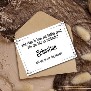 Peut inclure: Une carte blanche avec du texte noir demandant "avec des anneaux en main et en regardant bien, allez-vous nous aider à célébrer ? Sébastien, serez-vous notre porteur d'alliances ?"