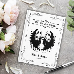 Könnte beinhalten: Ein weißes Journal mit einer Schwarzweißillustration von zwei Geistern, die sich in Herzform an den Händen halten. Der Text "Till We Are Ghosts" befindet sich über den Geistern und "Mike & Sophia 01-01-2025" unter den Geistern.