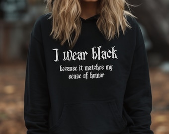 May include: Black hooded sweatshirt with the text "I wear black because it matches my sense of humor" in white gothic font. The sweatshirt has a front pocket and a drawstring hood. The model is wearing the sweatshirt.