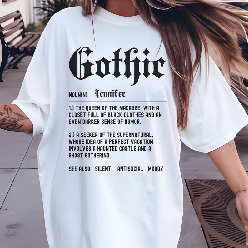 Puede incluir: Camiseta blanca con texto negro que dice "Gothic" en una fuente estilizada. El texto se define como "La reina de lo macabro, con un armario lleno de ropa negra y un sentido del humor a&uacute;n m&aacute;s oscuro. Un buscador de lo sobrenatural, cuya idea de unas vacaciones perfectas implica un castillo encantado y una reuni&oacute;n de fantasmas. Ver tambi&eacute;n: Silencioso, Antisocial, Melanc&oacute;lico."