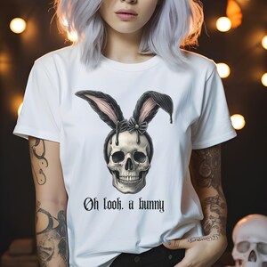 May include: White t-shirt featuring a black and white skull wearing bunny ears and a pink bow. The text "Oh look, a bunny" is printed below the skull.