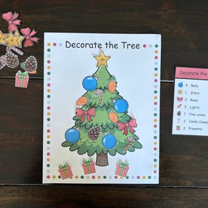May include: A Christmas-themed activity set with a decorated tree illustration and the text "Decorate the Tree." Includes cutouts of ornaments, bows, stars, pine cones, and presents. A list of items is also included.