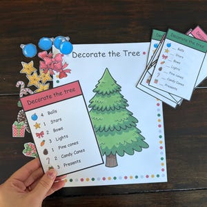 May include: A Christmas-themed activity set with a large illustrated tree, cards, and cutouts of ornaments. The cards list items like balls, stars, and bows. The cutouts include blue balls, gold stars, and red bows.
