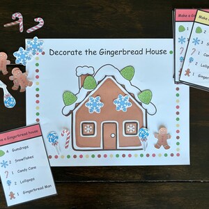 May include: A festive game featuring a gingerbread house illustration with decorative elements. The game includes cards with instructions, gingerbread men, candy canes, and lollipops. The text "Decorate the Gingerbread House" is displayed on the main card.