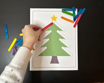 May include: A green Christmas tree outline with a yellow star on top. A hand is placing a red popsicle stick on the tree. There are other popsicle sticks in various colors scattered around the tree.