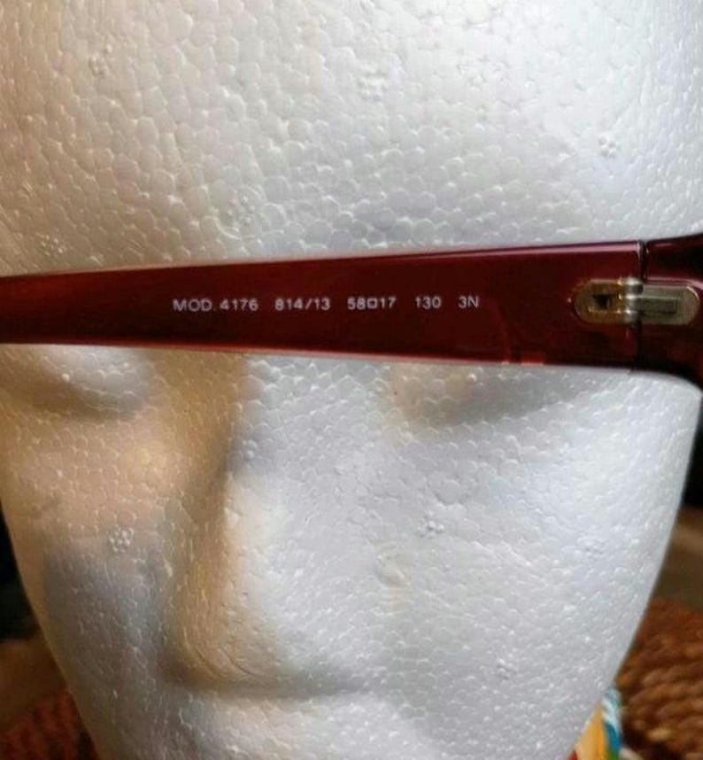 May include: Close-up of the temple of a pair of red eyeglasses. The text "MOD. 4176 814/13 58017 130 3N" is printed in white on the temple. The glasses are set against a white background.