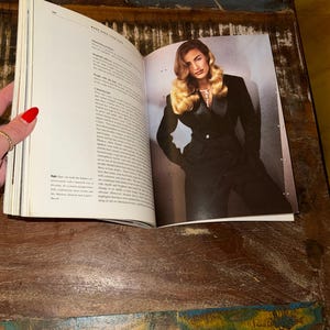 May include: A magazine page open to a spread featuring a woman with long blonde hair wearing a black suit jacket. The text on the page discusses the importance of hair and its role in fashion.