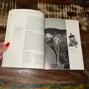 May include: A woman in a blue denim jacket and jeans walks along a rocky shoreline. The text "More Depth Than Cash" is visible on the page.