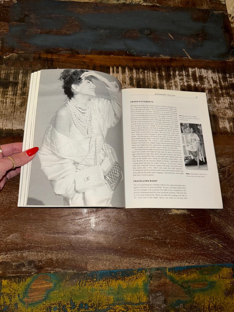 May include: A black and white photo of a woman wearing a white top, a pearl necklace, and a black quilted handbag. The text "Under Statements" and "Travelling Right" is visible on the page.
