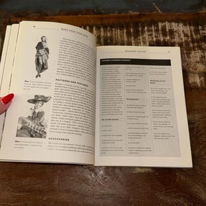 May include: Open book with a white background showing a page with the text "More Cash Than Cash" and a page with the text "Wardrobe Tactics" and "Ludinga Chambers Chooses". The book is open to a page with a black and white illustration of a man in a suit and a page with a black and white illustration of a woman in a dress.