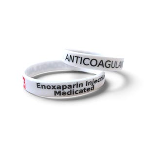 Può includere: Due braccialetti in silicone bianco con testo nero. Un braccialetto presenta la parola ANTICOAGULANT, mentre l'altro mostra il testo Enoxaparin Injection Medicated con una piccola icona quadrata rossa contenente un numero tre bianco.