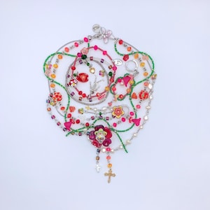 May include: A collection of colorful beaded necklaces with various charms, including flowers, skulls, and a cross. The necklaces are made with green, pink, and white beads.
