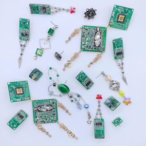 Puede incluir: Una colección de pendientes y tachuelas únicos, con placas de circuito verdes recicladas como punto focal. Los pendientes muestran varios diseños con cuentas colgantes, cristales y detalles metálicos. La colección incluye tachuelas y pendientes colgantes con una estética moderna inspirada en la tecnología.