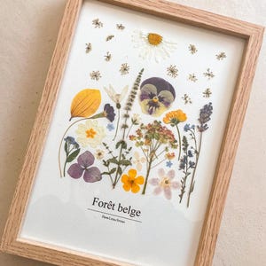 Composition botanique de fleurs et feuilles pressées dans un cadre en bois clair