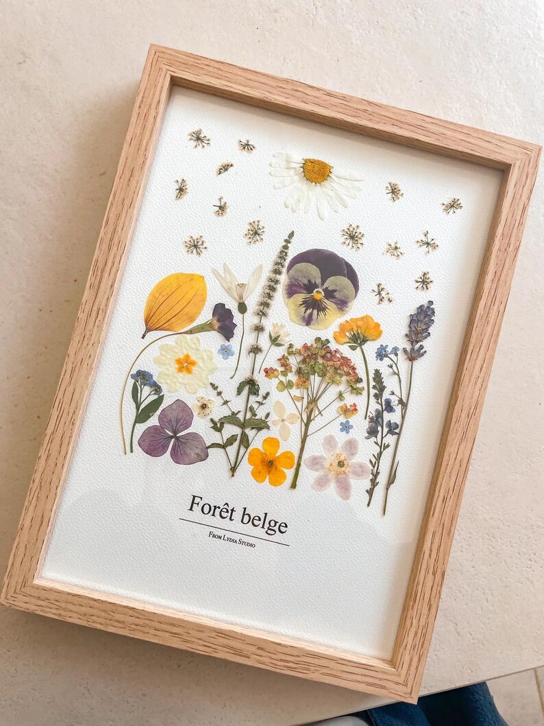 Composition botanique de fleurs et feuilles pressées dans un cadre en bois clair