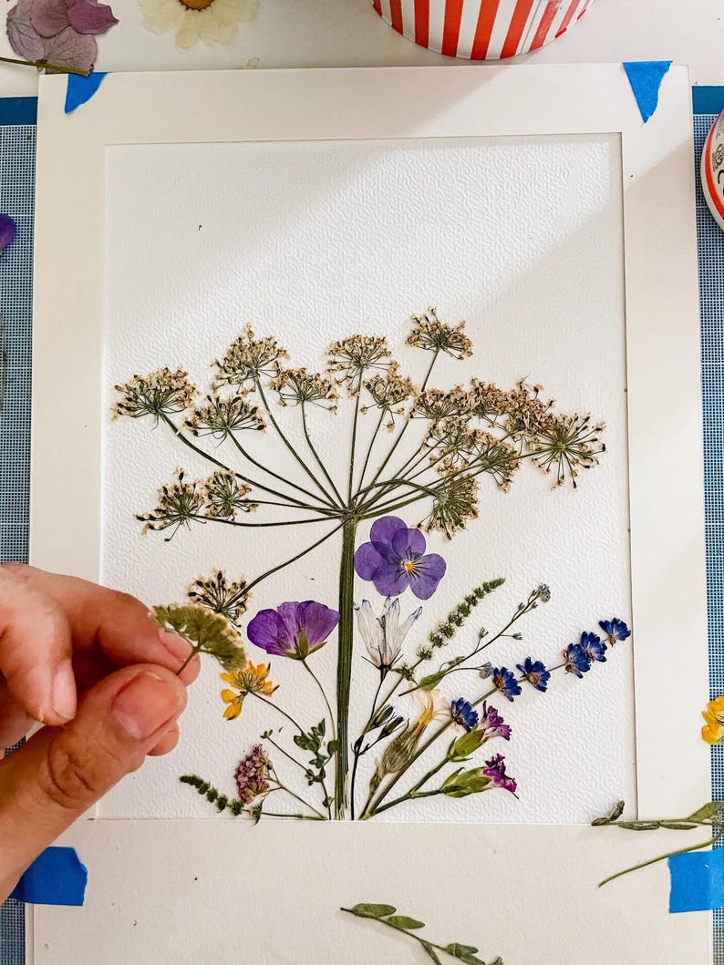 La main de Lydia place les fleurs pressées sur le papier de « Printemps ! »