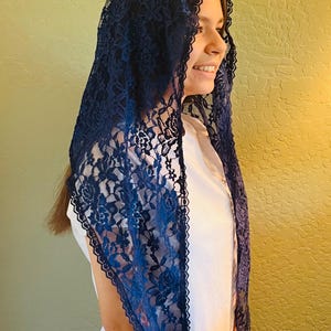 Puede incluir: Un velo de encaje azul marino con un diseño floral. El velo está drapeado sobre la cabeza y los hombros, con un borde festoneado. La persona lleva una camisa blanca.