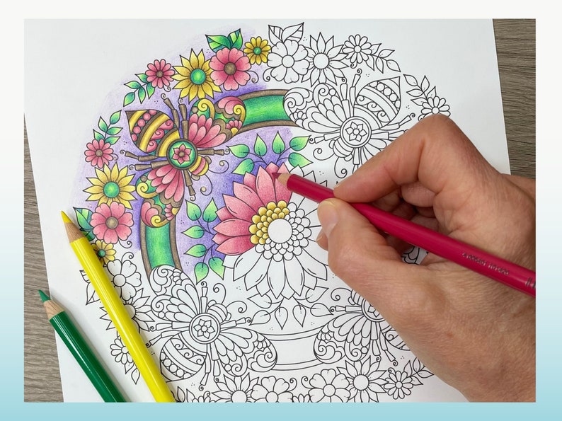 May include: A close-up of a hand coloring a detailed mandala design with colored pencils. The mandala features a bee, flowers, and leaves. The design is partially colored in shades of pink, yellow, and green.