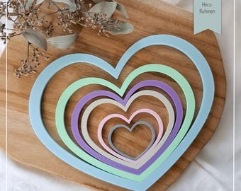 Puede incluir: Un conjunto de seis cortadores de galletas con forma de corazón en varios colores pastel, incluyendo azul claro, verde, morado, beige, rosa y gris. Los cortadores están dispuestos en un patrón anidado, con el cortador más grande en la parte inferior y el más pequeño en la parte superior. Los cortadores están sobre una superficie de madera. STL-Datei: Herz-Rahmen