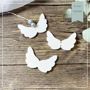 Può includere: Tre ornamenti ad ali d'angelo bianche su uno sfondo di legno. Un set di ali è collegato a una corda con due perline. Il testo "STL-Datei: Engelsflügel" è in una scatola turchese. Le ali sono realizzate in materiale liscio.