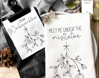 May include: A white kitchen towel with black embroidery of a mistletoe sprig and the text "Meet me under the mistletoe".