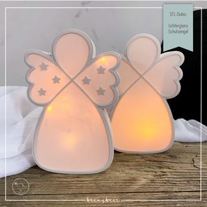 Può includere: Due luci notturne a forma di angelo con una morbida luce rosa. Le ali presentano ritagli a forma di stella. Il testo sull'immagine recita "STL-Datei: Lichterglanz Schutzengel". Le luci sono su una superficie di legno.
