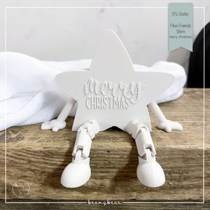 Könnte beinhalten: Eine weiße sternförmige Weihnachtsdekoration mit beweglichen Beinen und Armen. Die Worte "Merry Christmas" sind auf dem Stern geprägt. Die Dekoration befindet sich auf einer Holzoberfläche.