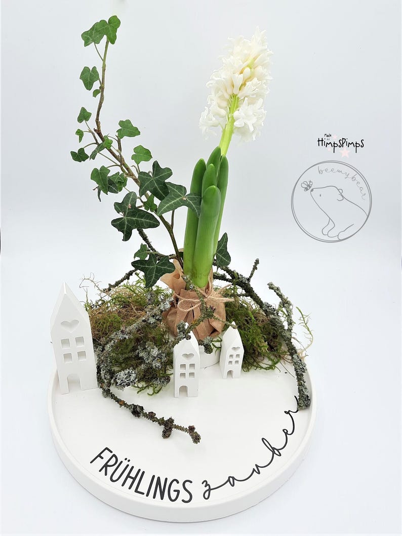 以下が含まれることがあります： 白いヒヤシンスの花の飾り付け。白い陶器の皿に、