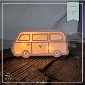 Può includere: Una luce notturna a forma di camper di colore pesca, illuminata dall'interno. Il furgone presenta dettagli a forma di cuore e finestre rettangolari. Il testo "STL-Datei: Lichterglanz Bus" è su uno striscione turchese. Poggia su una superficie di legno.