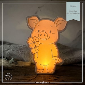 Pode incluir: Uma luminária de tons quentes e brilhantes em forma de porquinho de desenho animado segurando um trevo de quatro folhas. A superfície apresenta contornos gravados dos traços do porco. Uma etiqueta azul clara exibe o texto: STL-Datei: Lichterglanz Glücksschweinchen.