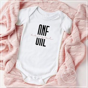 May include: White baby onesie with black text that reads "ONE derful  UIL".