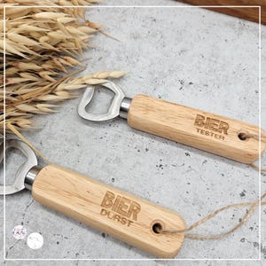 May include: Two wooden bottle openers with metal bottle opener heads. One opener has the text "BIER TESTER" engraved on the wood. The other opener has the text "BIER DURST" engraved on the wood.