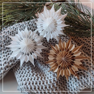 May include: Three paper snowflakes, one white, one brown, and one white with a brown center, are arranged on a gray knitted surface.