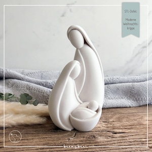 May include: A smooth, matte white figurine depicting a stylized nativity scene with three figures. The text "STL-Datei: Moderne Weihnachtskrippe" is visible in the upper right corner. The sculpture features fluid, abstract shapes representing a family.