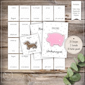 Könnte beinhalten: Eine Sammlung weißer Karten mit schwarzen Punkten und deutschem Text, die verschiedene Designs zeigen, darunter ein rosa Schweinchen-Magnet und ein Dackel-Magnet. Die Karten sind auf einer Holzoberfläche angeordnet.