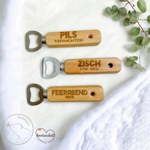 May include: Three wooden bottle openers with different sayings engraved on them. The top opener says "Pils Vernichter", the middle opener says "Zisch und Weg", and the bottom opener says "Feierabend Bier".