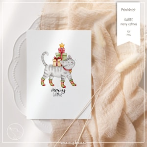 Puede incluir: Una tarjeta de felicitación blanca presenta un gato gris que lleva regalos envueltos, una estrella y el texto "merry catmas". El gato lleva un collar rojo y calcetines a rayas. La tarjeta está sobre un plato blanco con un fondo de tela beige.