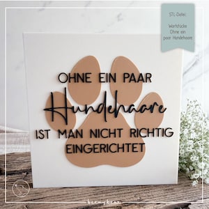 May include: A white square sign featuring a large tan paw print in the center. Black text reads: OHNE EIN PAAR Hundehaare IST MAN NICHT RICHTIG EINGERICHTET. A small light green tag in the top right corner displays the text: STL-Datei: Wortstücke Ohne ein paar Hundehaare.