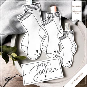 Puede incluir: Tres formas de calcetines negros y blancos con corazones en los dedos. Una etiqueta blanca con texto negro que dice "STATT SOCKEN" con un corazón debajo del texto. El texto "ITH-Stickdatei: Geldgeschenk Socken" está en la esquina superior derecha de la imagen.