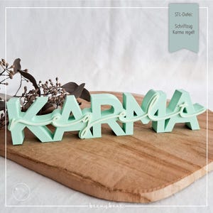 Puede incluir: Una pieza de arte de palabras "Karma" verde menta con una superposición de "g" en cursiva, exhibida en una tabla de cortar de madera. El texto "STL-Datei: Schriftzug Karma regelt" está en un rectángulo verde azulado en la esquina superior derecha.