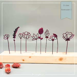 May include: A set of ten 3D printed flowers in a deep burgundy color, arranged on a wooden base. The flowers are all different shapes and sizes, and they are all made of a thin, wire-like material. The flowers are labeled "STL-Datei: Blumenzauber 2".