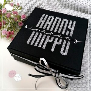 May include: Black gift box with a silver glitter "Happy Birthday" inscription on the lid. The box is tied with a black and silver ribbon and decorated with silver sequins.