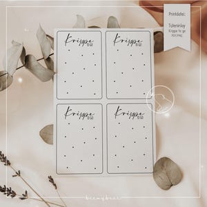 Puede incluir: Cuatro tarjetas rectangulares blancas con el texto "Krippe to go" en fuente manuscrita, cada una con una cuadrícula de pequeños puntos negros. Una pequeña etiqueta dice "Printdatei: Tüteninlay Krippe to go PDF/PNG". Las tarjetas están sobre un fondo neutro.