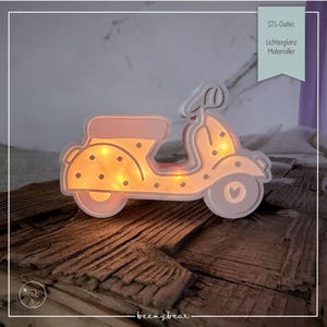 Può includere: Decorazione a forma di scooter illuminato, nei toni del rosa e crema, con un motivo a pois sul lato. Lo scooter ha un dettaglio a forma di cuore sulla ruota ed è illuminato da luci gialle calde. Il testo "STL-Datei: Lichterglanz Motorroller" è visibile.