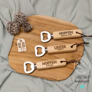 May include: Three wooden bottle openers with metal bottle opener parts. The bottle openers are engraved with the text "Hoppen Smoothie", "Unter Hopft", and "Hoppen Konig".