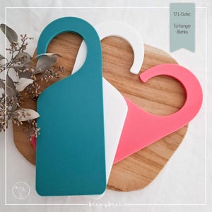 Könnte beinhalten: Drei Türhänger in Teal, Weiß und Pink, angeordnet auf einer Holzoberfläche. Der tealfarbene Hänger befindet sich im Vordergrund, mit einem gebogenen Oberteil und einem rechteckigen Körper. Die weißen und pinkfarbenen Hänger befinden sich dahinter. Der Text auf dem Bild lautet "STL-Datei: Turhanger Blanko."