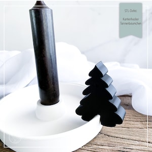 Può includere: Un portacandele in ceramica bianca con una candela marrone scuro e un ornamento nero a forma di albero di Natale. Il portacandele ha una base circolare e un centro rialzato per la candela. L'albero è posto sul lato del supporto.