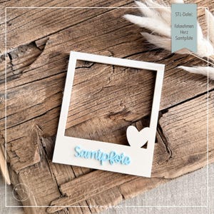 May include: A white square photo frame with a cutout heart shape in the bottom right corner and the light blue script text Samtpfote embossed on the bottom border. The frame is designed for 3D printing as indicated by the text STL-Datei.